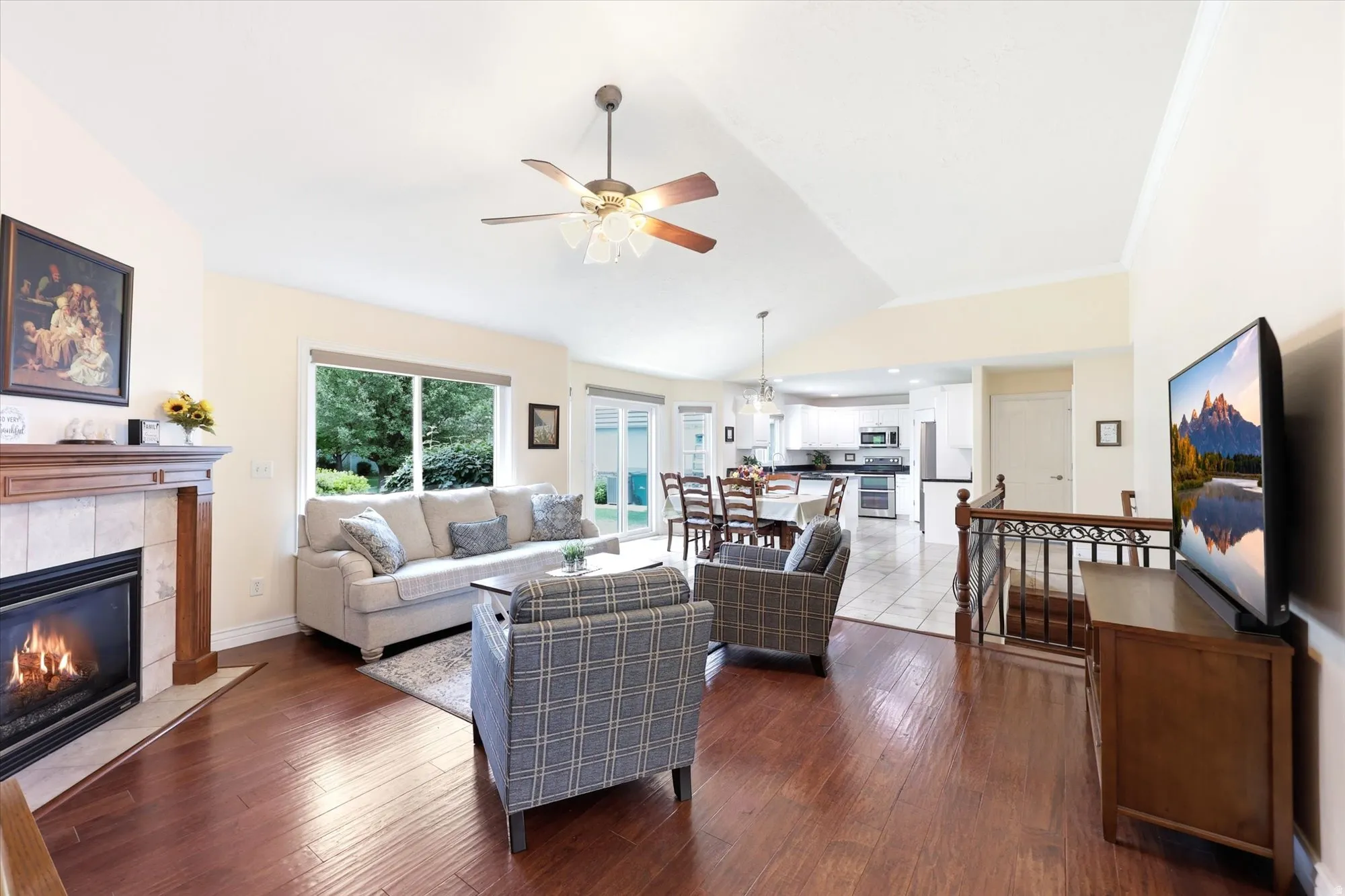 Spacious living area featuring wood-finish flooring, a tiled fireplace with a wood mantel, and an elevated ceiling with a ceiling fan