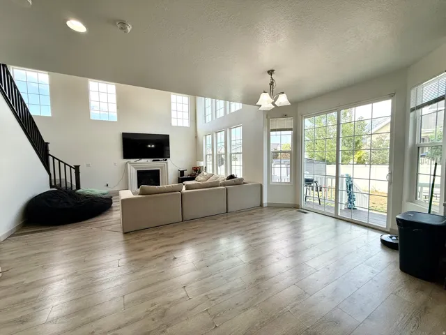 Spacious living area featuring high ceilings, wood-finish flooring, a fireplace with a white mantel, and multiple large windows