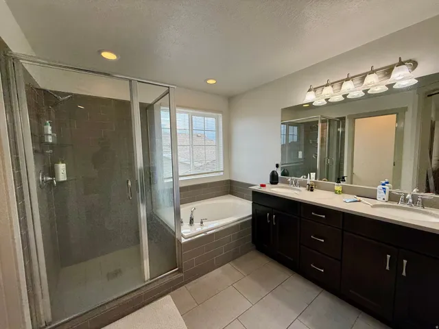 Spacious bathroom featuring a dual vanity, undermount sinks, a large soaking tub with subway tile surround, a separate glass-enclosed shower, and recessed lighting