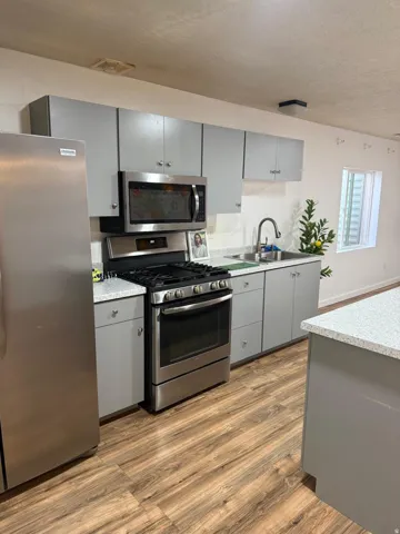 Kitchen featuring stainless steel appliances, gray cabinetry, wood-finish flooring, light-toned countertops, and a kitchen island