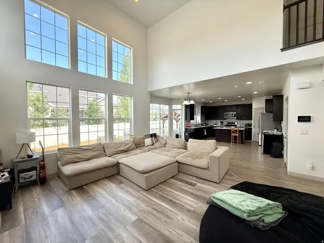 Vaulted living area with expansive window wall, wood-finish flooring, and an open-concept layout leading to a kitchen with dark cabinetry and stainless steel appliances