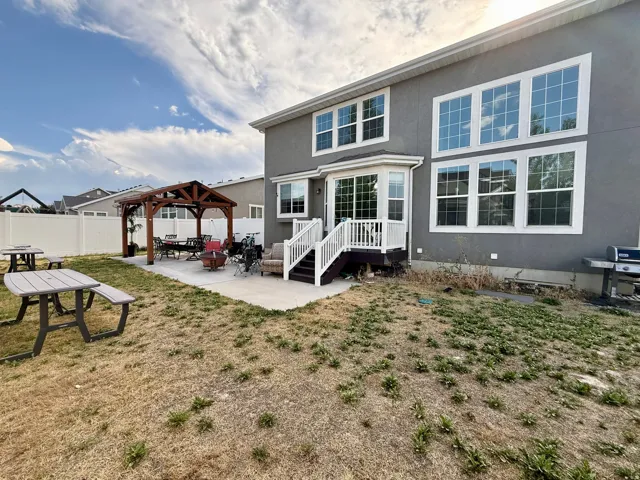 Spacious backyard featuring a concrete patio, a wooden pergola, and a white picket fence