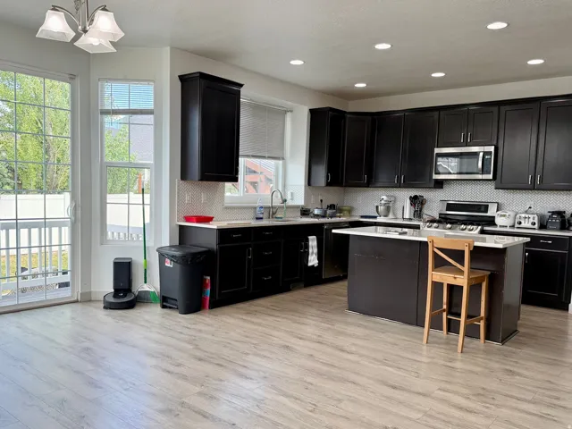 Open-concept kitchen featuring dark cabinetry, stainless steel appliances, a center island with countertop seating, and light wood-finish flooring