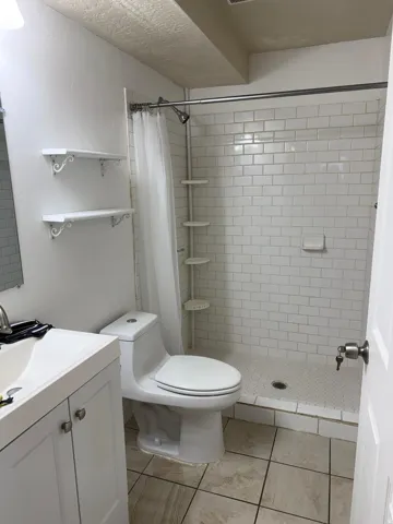 Bathroom featuring a white subway tile shower enclosure with a mosaic tile floor, ceramic tile flooring, a white vanity with integrated sink, and an exposed pipe ceiling