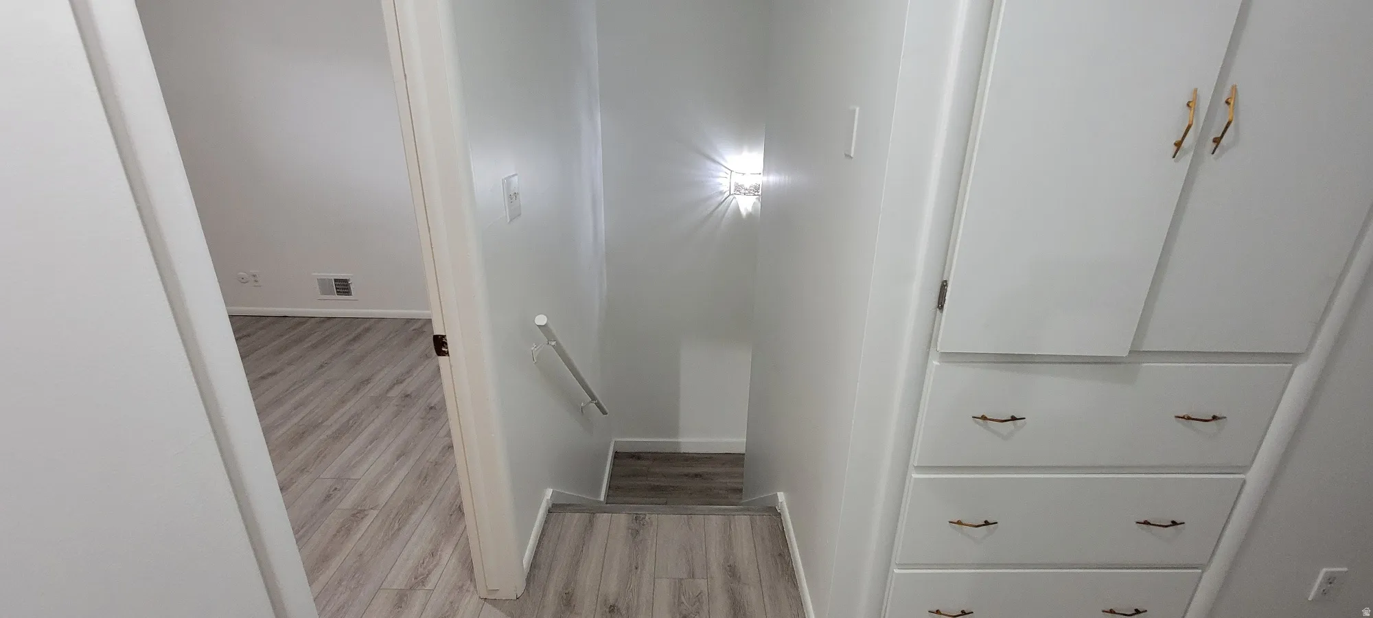 Recessed staircase with integrated wall sconce lighting, featuring a handrail and built-in white cabinetry with brass-tone hardware