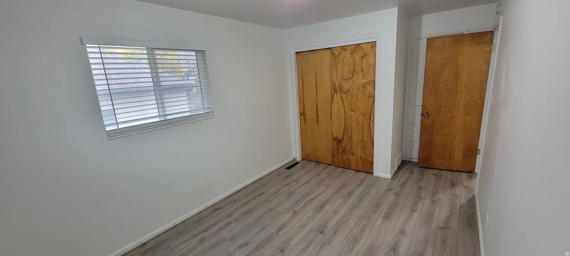 Room featuring light wood-finish flooring, white painted walls, and a window with horizontal blinds
