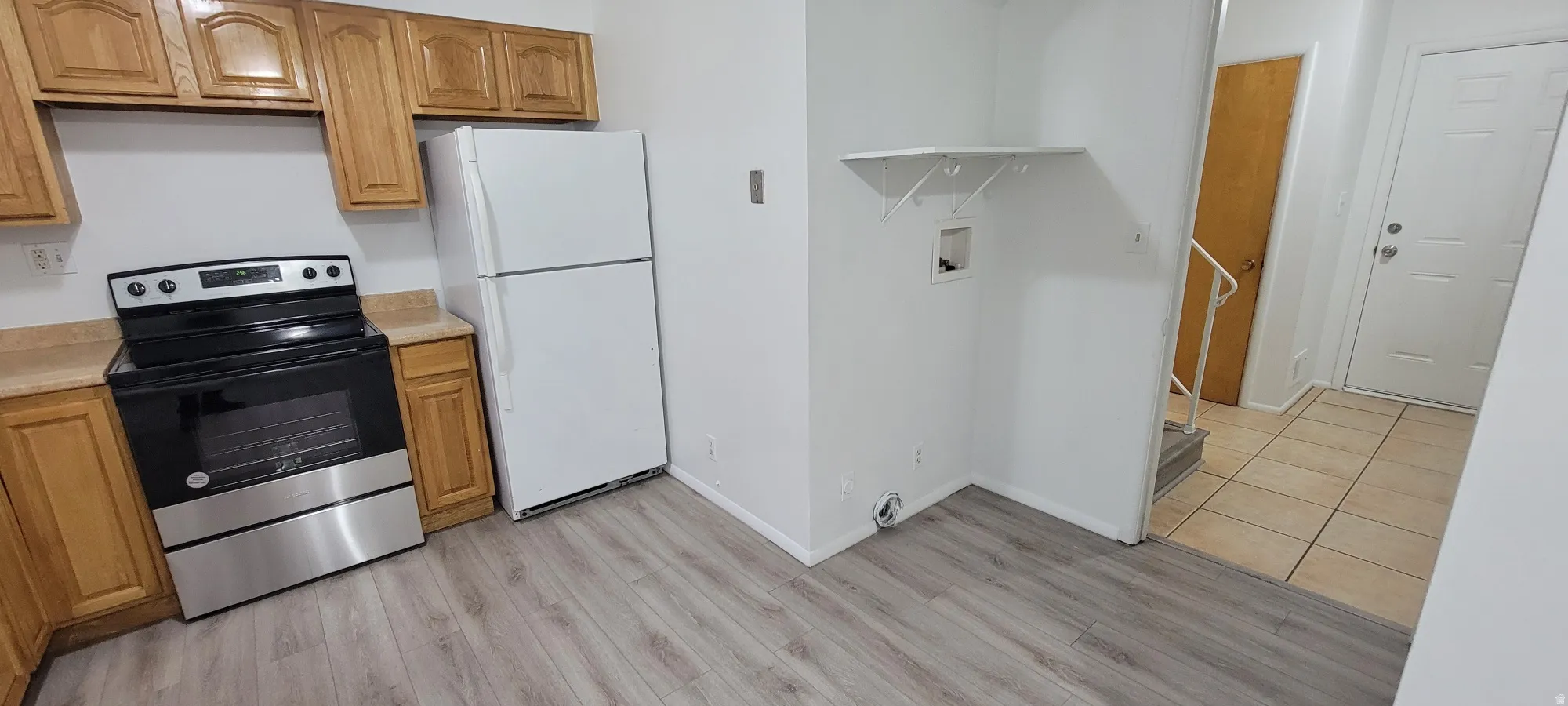 Kitchen area featuring wood-finish laminate flooring, light wood cabinetry, and a stainless steel and black range