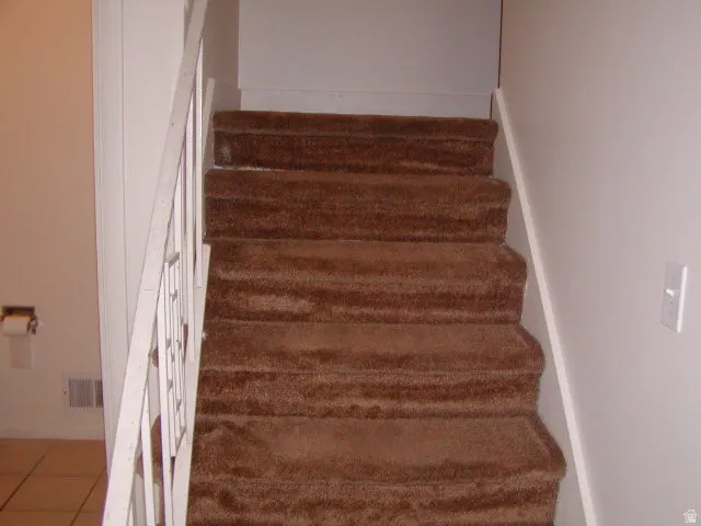 Carpeted staircase featuring a white railing and neutral wall tones