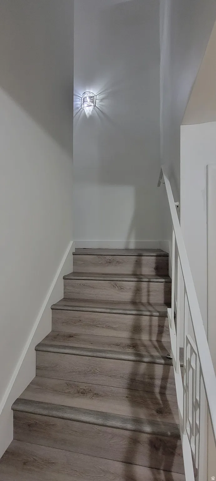 Staircase featuring wood-finish treads and risers, white wall paneling, and a white handrail with decorative balusters