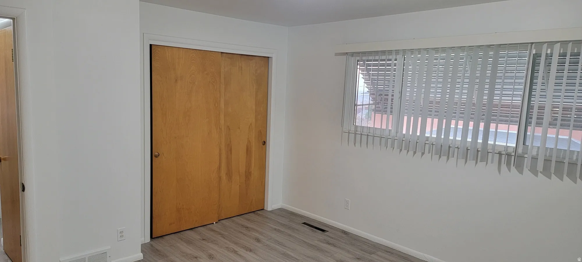 Room featuring wood-finish flooring, a double-door closet with wood doors, and a window with vertical blinds