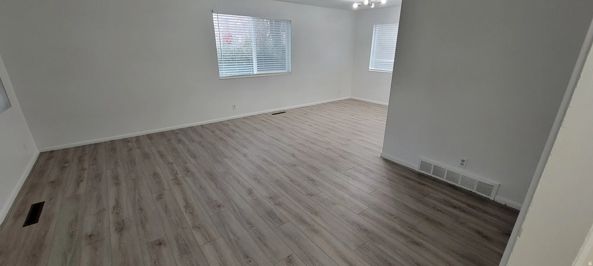 Spacious interior featuring wood-finish flooring, white baseboards, and multiple windows with blinds