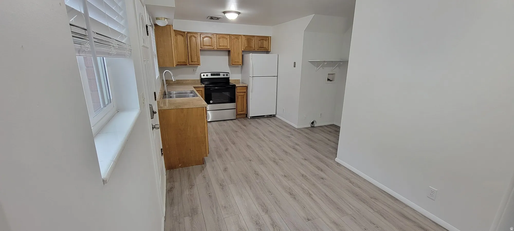 Kitchen area featuring wood-finish flooring, light wood cabinetry, laminate countertops, and a double basin stainless steel sink