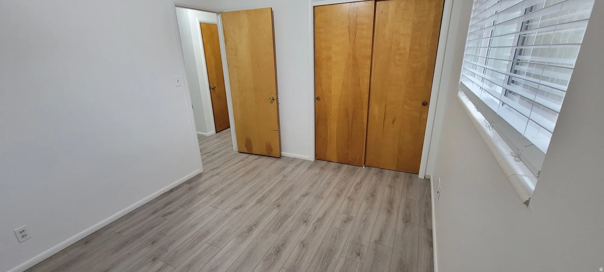 Room featuring light wood-finish flooring, white painted walls, and a window with horizontal blinds