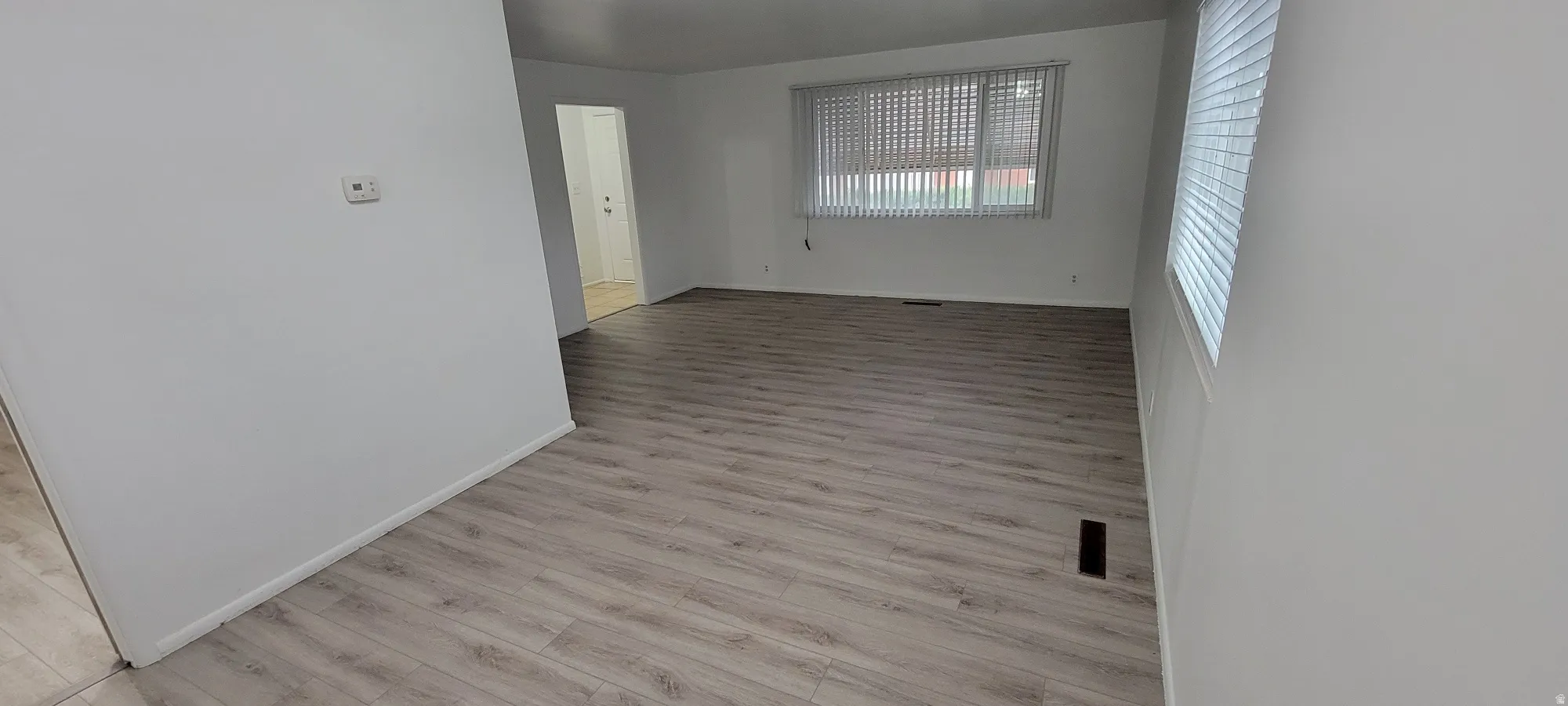 Spacious room featuring light wood-finish flooring, white baseboards, and a neutral wall color