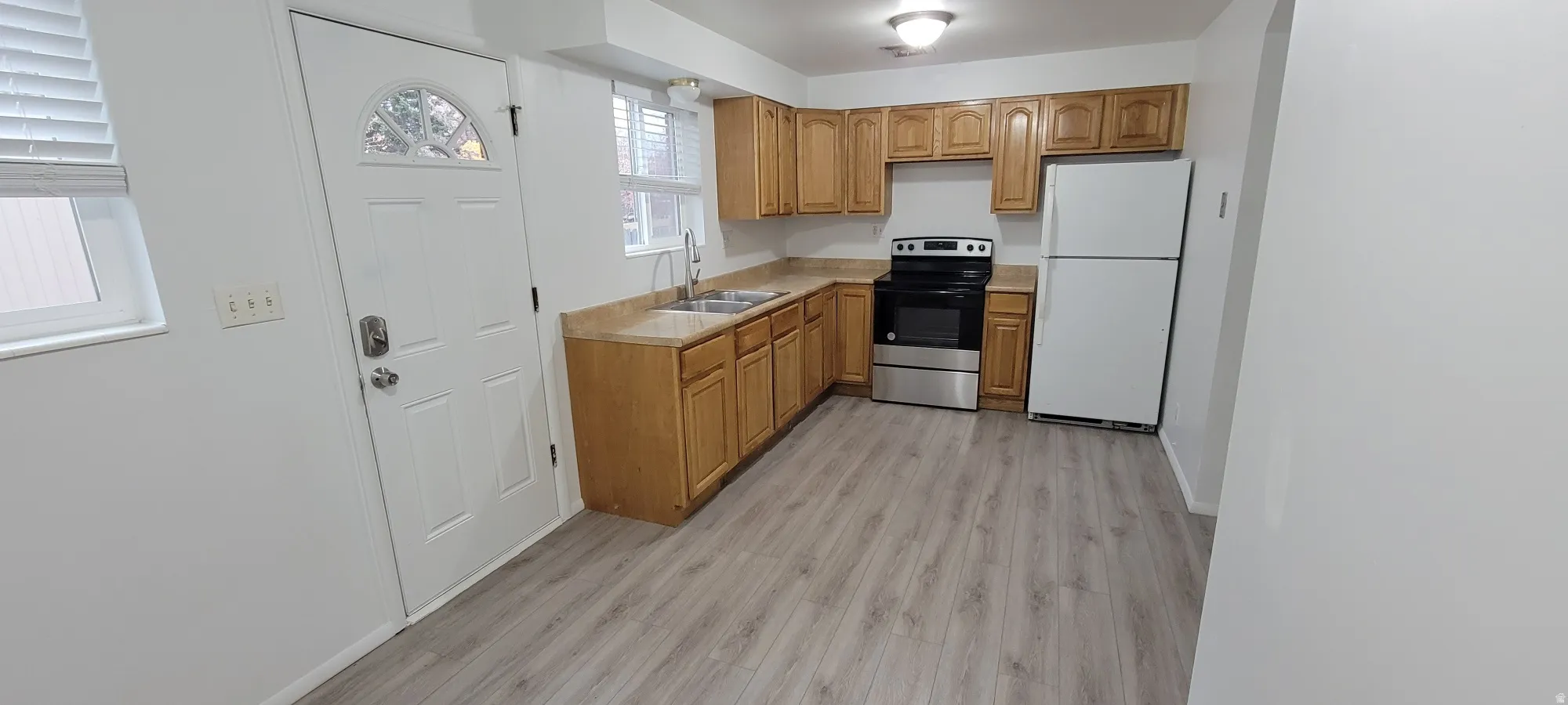 Kitchen featuring light wood-finish cabinetry, a stainless steel electric range, a white refrigerator, and wood-finish flooring