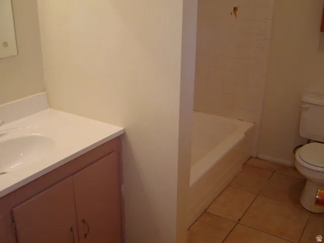 Bathroom featuring a single vanity with an integrated sink and light-toned countertop, a built-in bathtub with tiled surround, and ceramic tile flooring