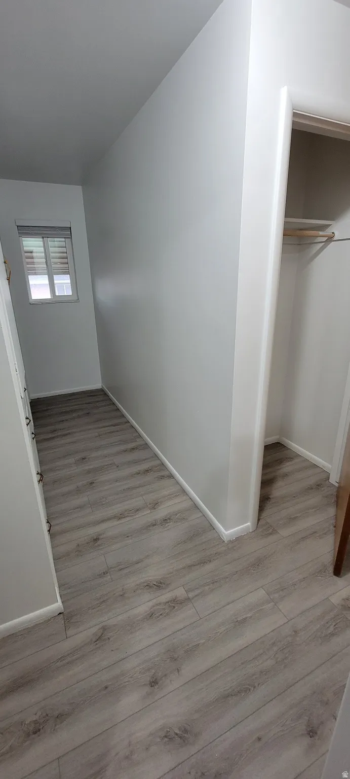 Hallway featuring wood-finish flooring, light grey walls, white trim, and an open closet with a hanging rod