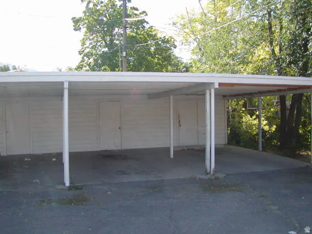 Spacious carport featuring a white metal roof and support columns, concrete flooring, and three exterior storage doors