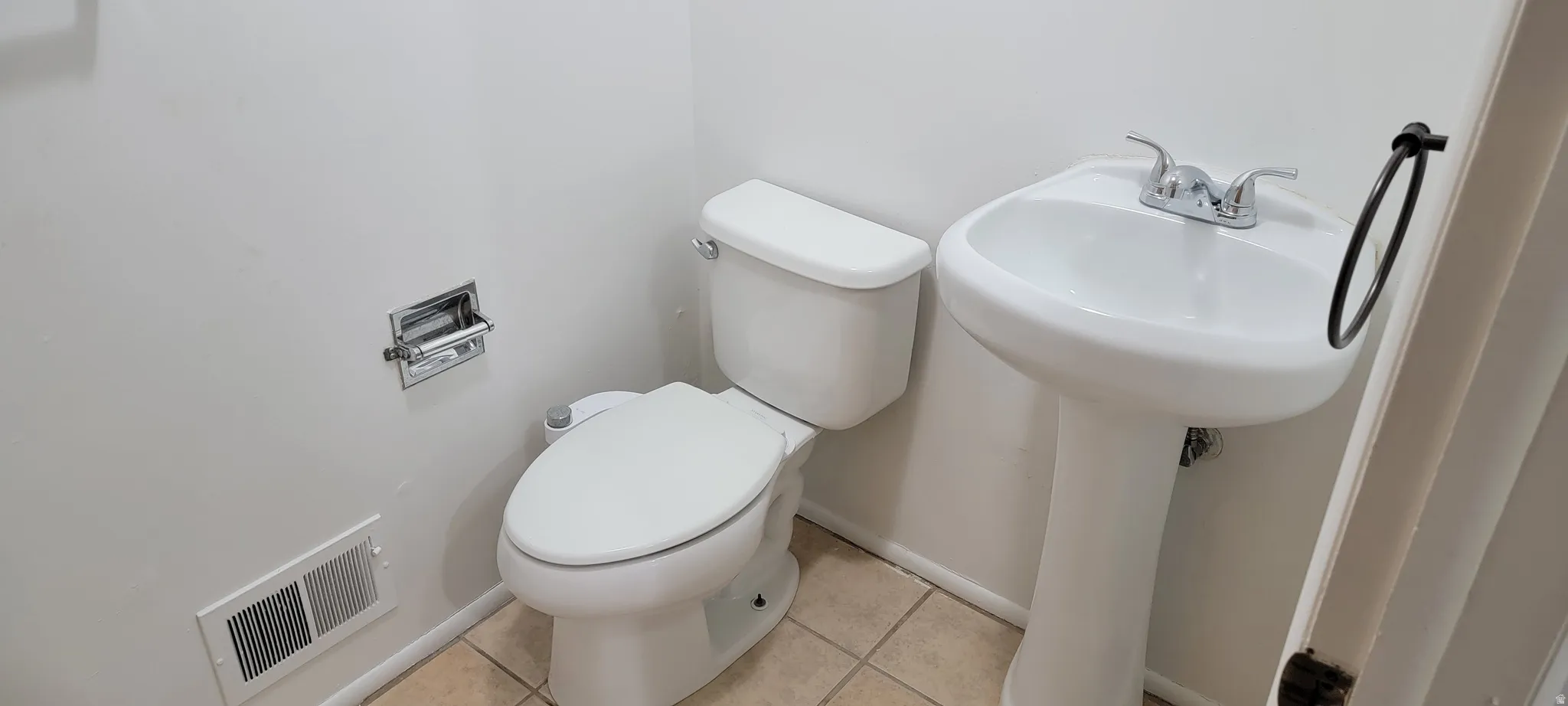 Pedestal sink with chrome faucet, complemented by a white toilet and neutral-toned floor tiling
