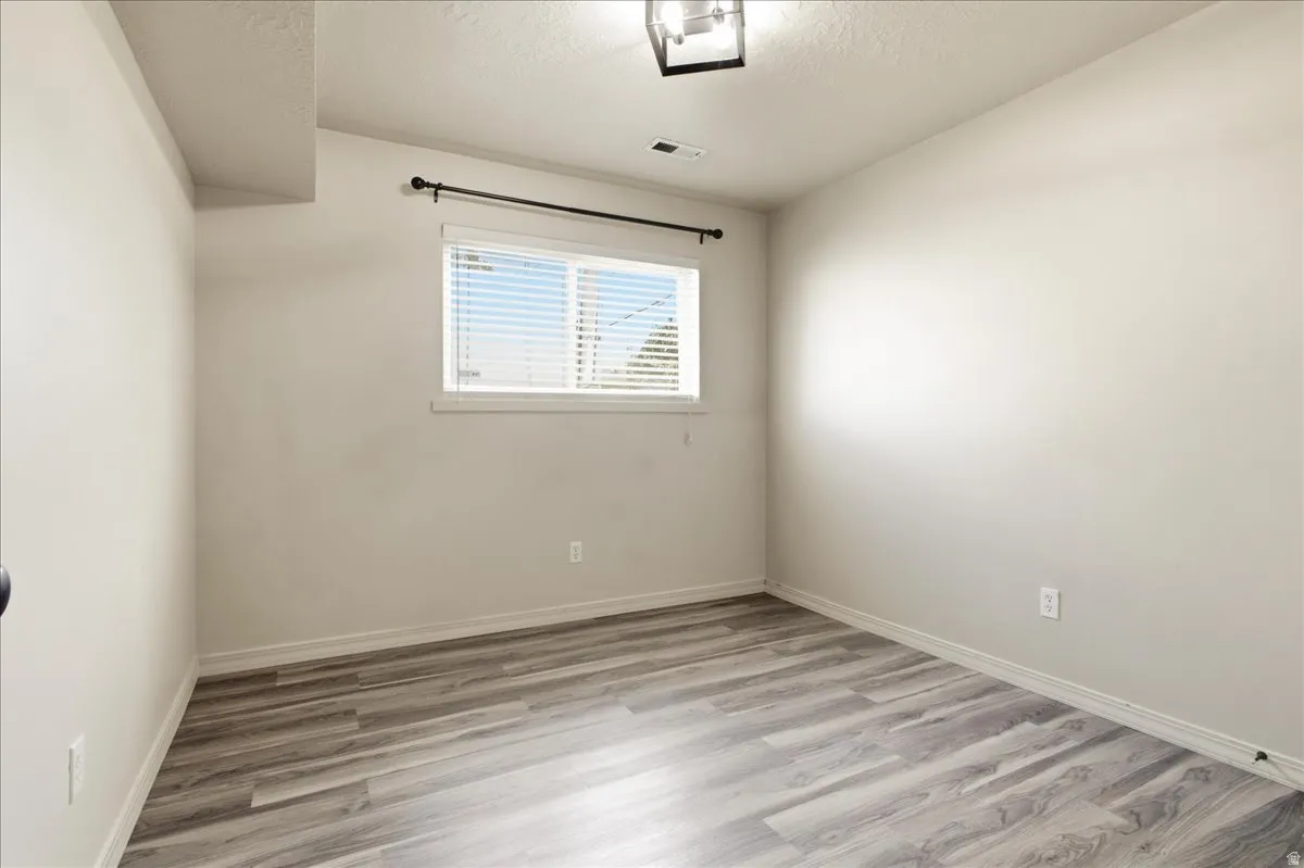 Room featuring wood-finish flooring, a window with blinds, and a ceiling-mounted light fixture