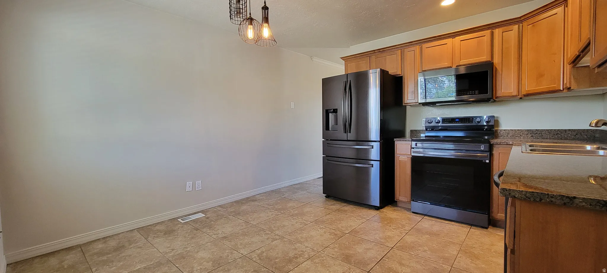 Kitchen area featuring a suite of black stainless steel appliances, wood cabinetry, stone countertops, and tile flooring