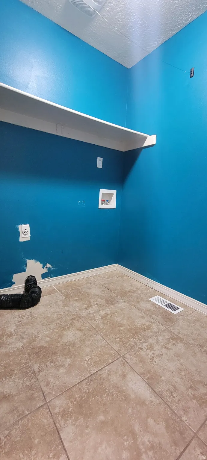 Laundry area featuring tile flooring, a white wall shelf, and electrical outlets