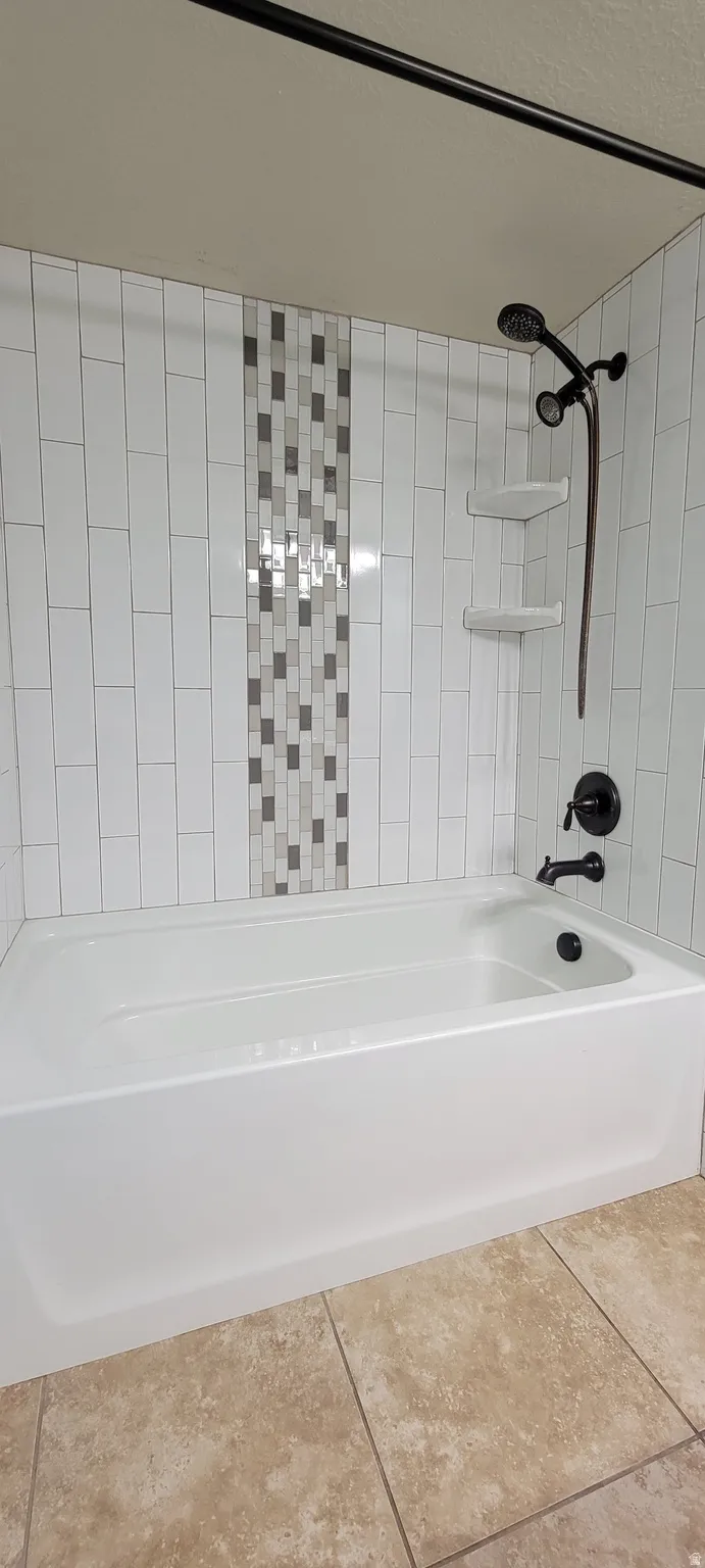 Bathtub with white subway tile surround, mosaic accent tile, dark bronze shower fixtures, and neutral-toned floor tile