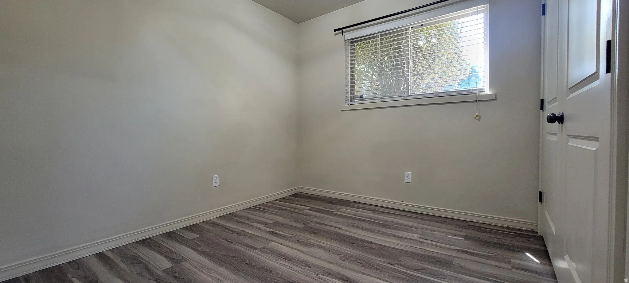 Interior room featuring wood-finish flooring, light-toned walls, and a window with blinds