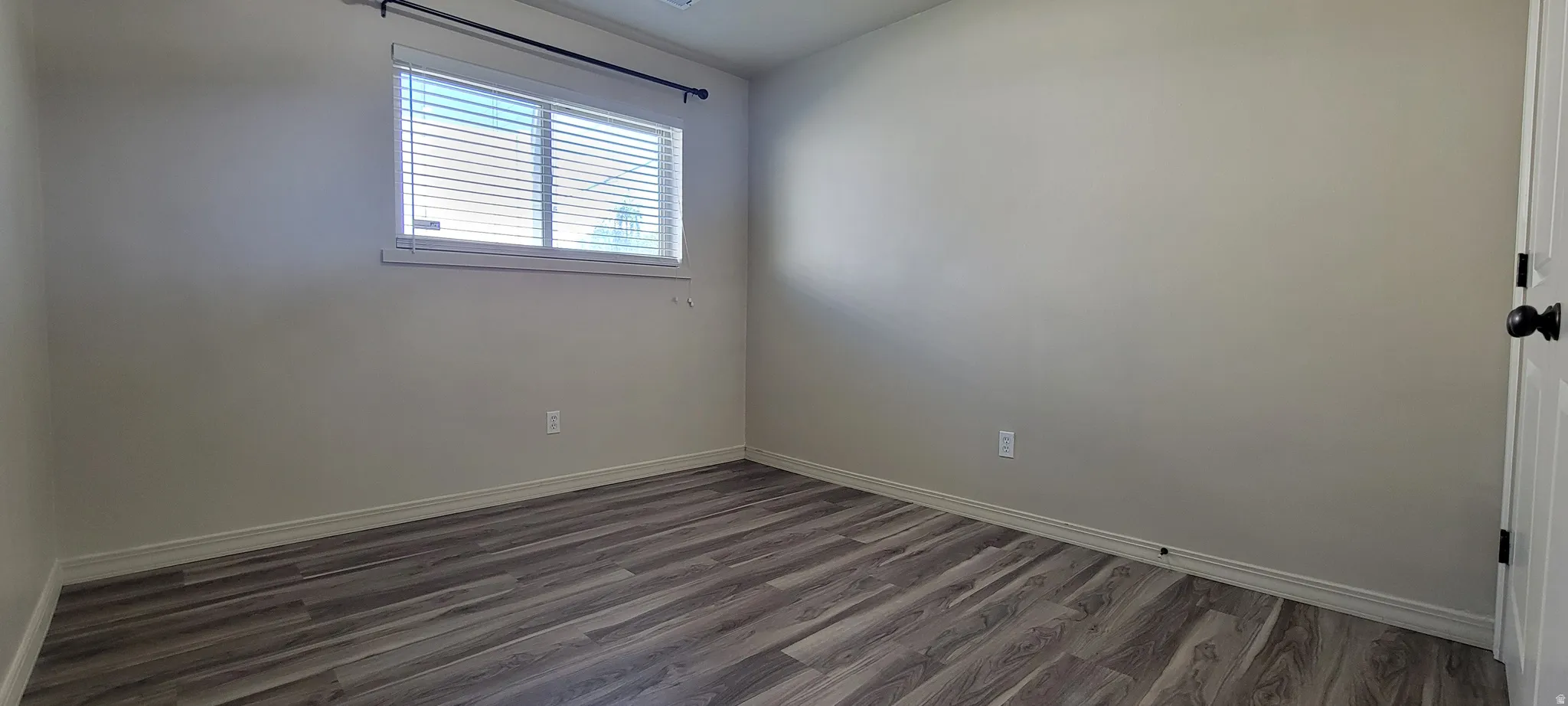 Room featuring wood-finish flooring, a double window with blinds, and light-colored walls