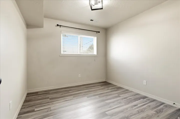 Room featuring wood-finish flooring, a window with blinds, and a ceiling-mounted light fixture