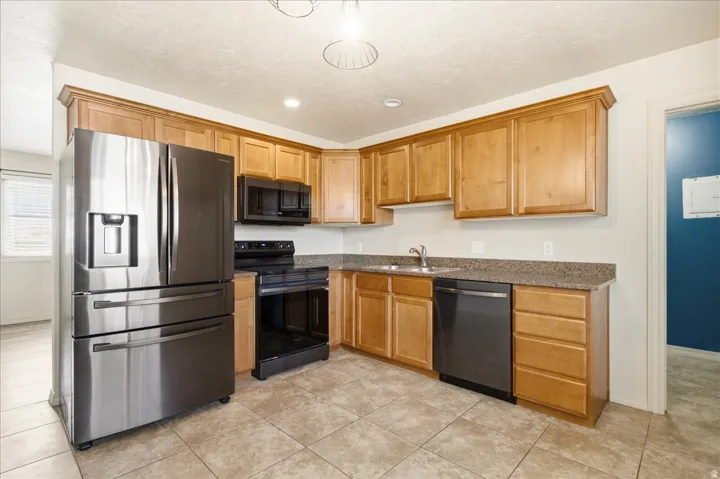 Kitchen featuring wood cabinetry, stainless steel appliances, a black electric range, a black dishwasher, and tile flooring