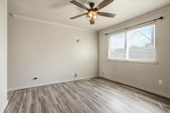 Crown molding, wood-finish flooring, ceiling fan with integrated lighting, window with blinds, and white trim