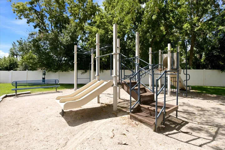 Outdoor recreation area featuring a play structure with slides and stairs, sand ground cover, a metal bench, and a privacy fence