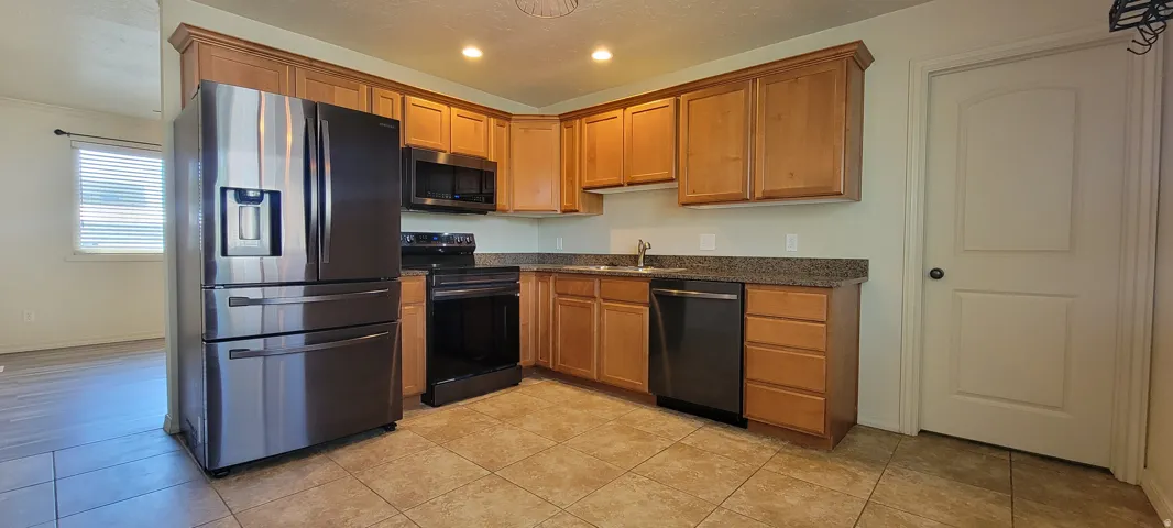 Kitchen featuring stainless steel refrigerator, black finished appliances, wood cabinetry, stone countertops, and tile flooring