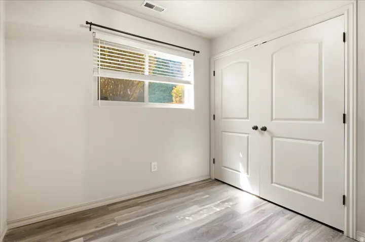 Wood-finish flooring with white baseboards, window with white blinds, and a double-door closet with dark hardware