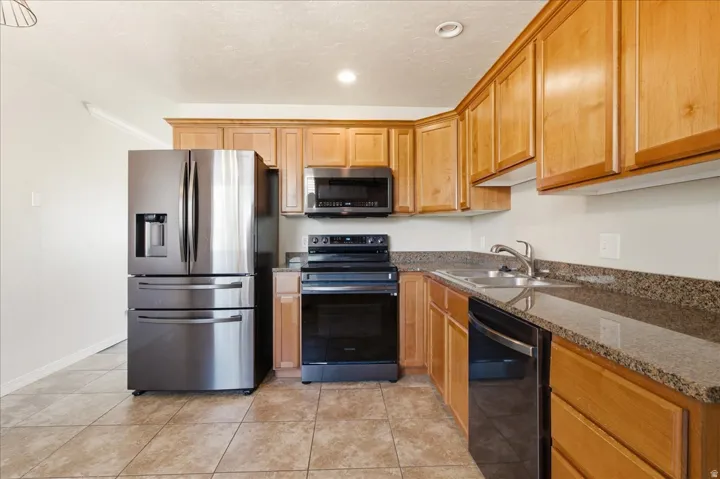 Stainless steel refrigerator, built-in microwave, dark-toned electric range, stainless steel dishwasher, and a double basin sink