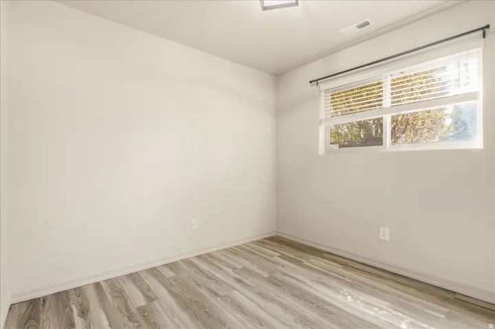 Wood-finish flooring with neutral wall tones and a single window featuring horizontal blinds