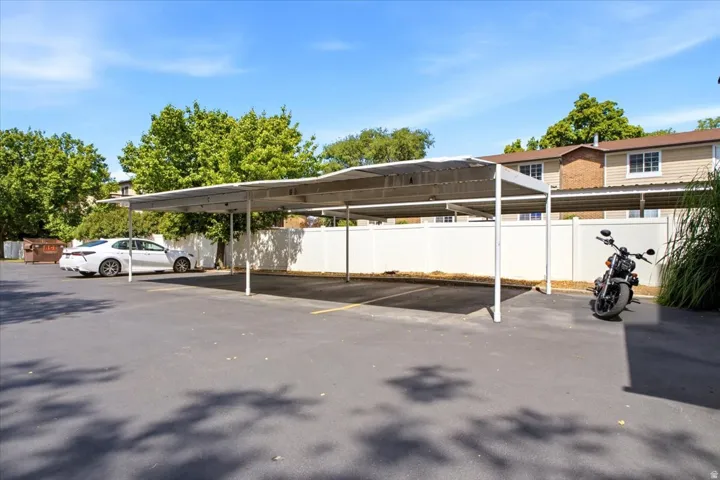 Paved parking area featuring a multi-stall carport structure and a white privacy fence