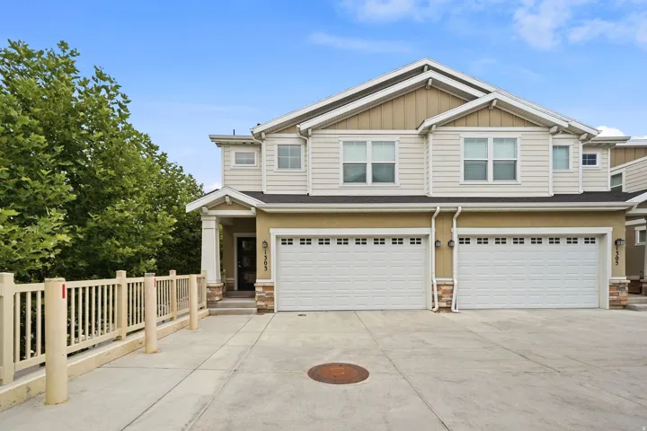 Contemporary townhome exterior featuring two attached garage doors, light-colored siding, and a covered entry porch with stone accents