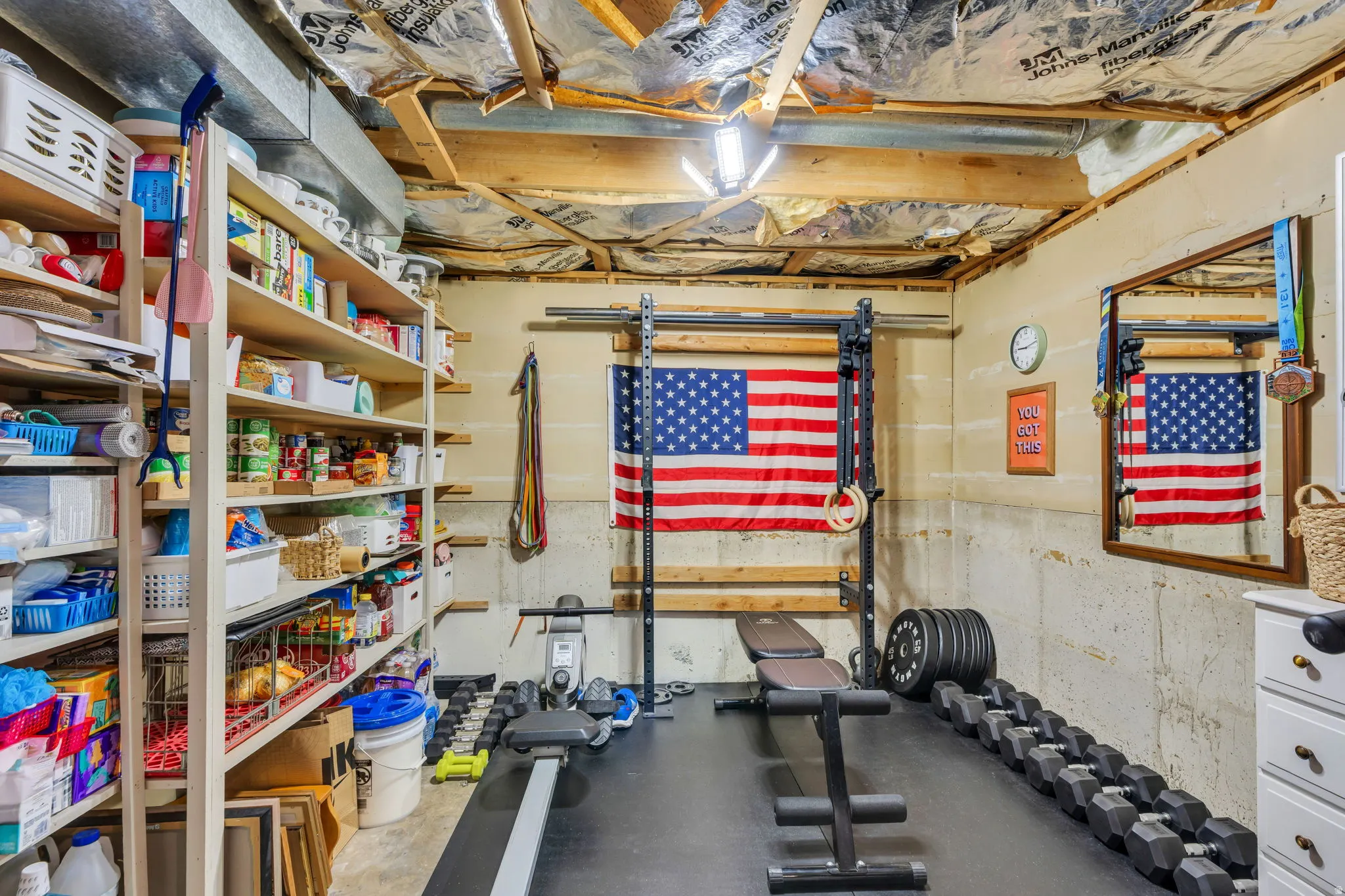 Multi-functional basement area featuring extensive built-in shelving, exposed ceiling joists, and a durable rubber mat flooring