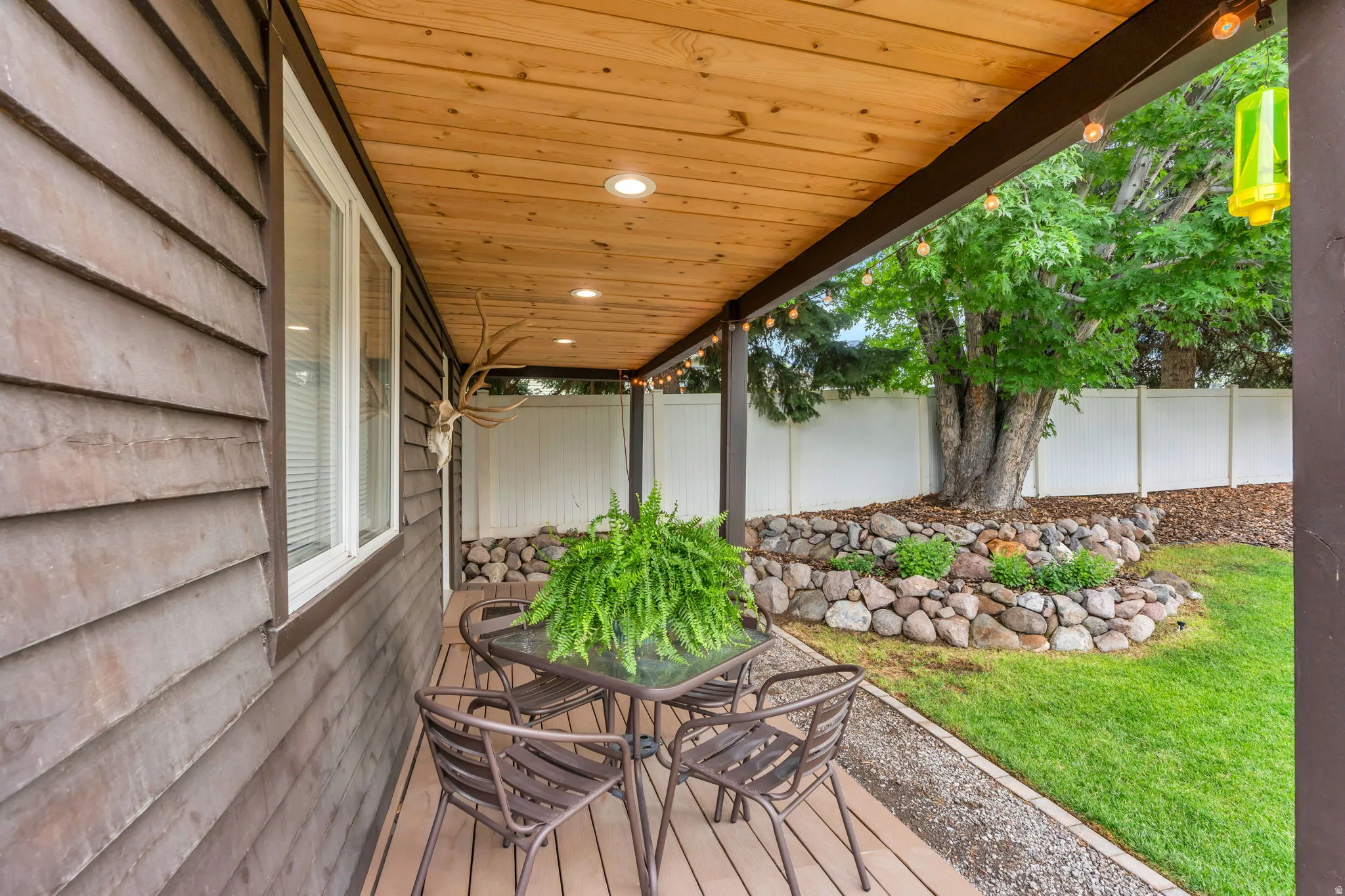 Covered patio featuring a wood-finish ceiling with recessed lighting, brown siding, and a white privacy fence