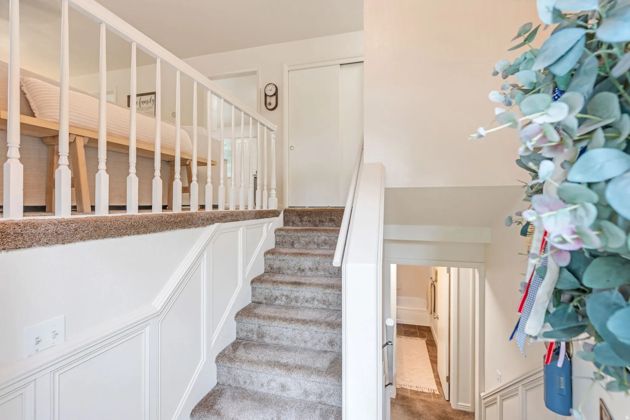 Carpeted staircase with white balusters and wainscoting