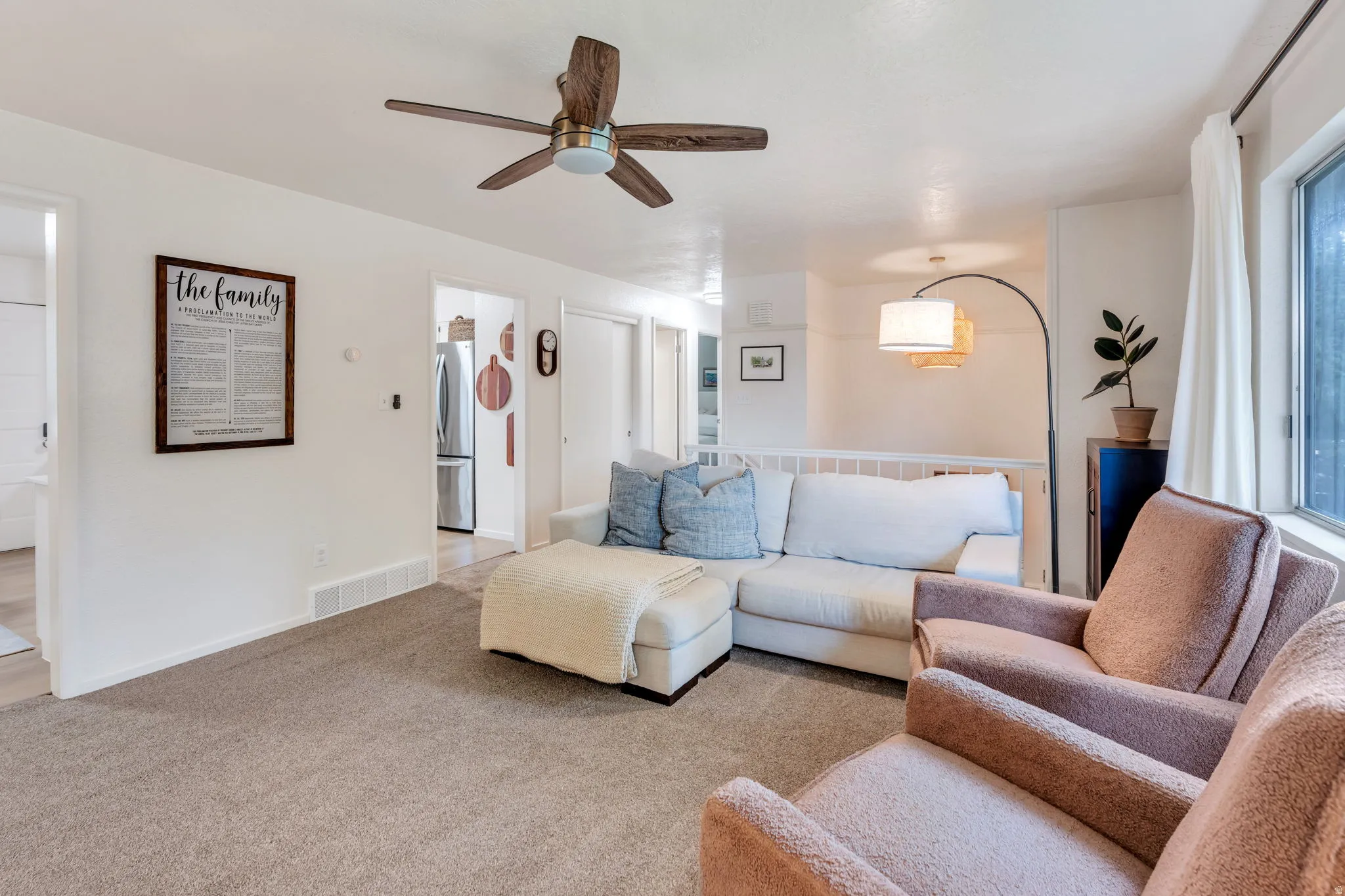 Carpeted living space featuring a wood-finish ceiling fan and white walls