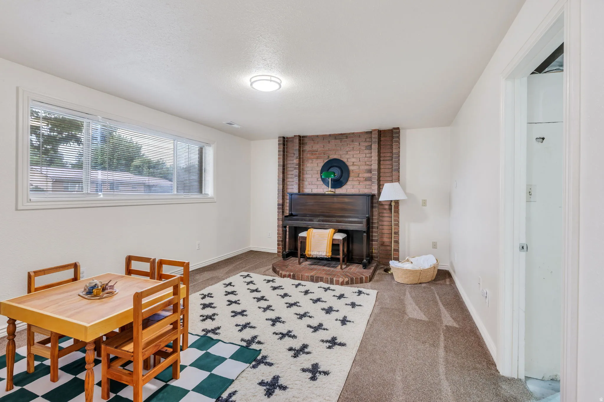 Spacious room featuring a brick-clad fireplace with a raised hearth, light neutral carpeting, and a large multi-pane window
