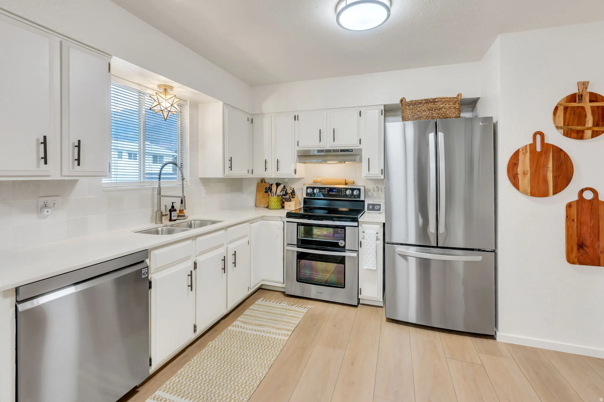 Kitchen featuring white cabinetry, light countertops, wood-finish flooring, stainless steel appliances, and a tile backsplash