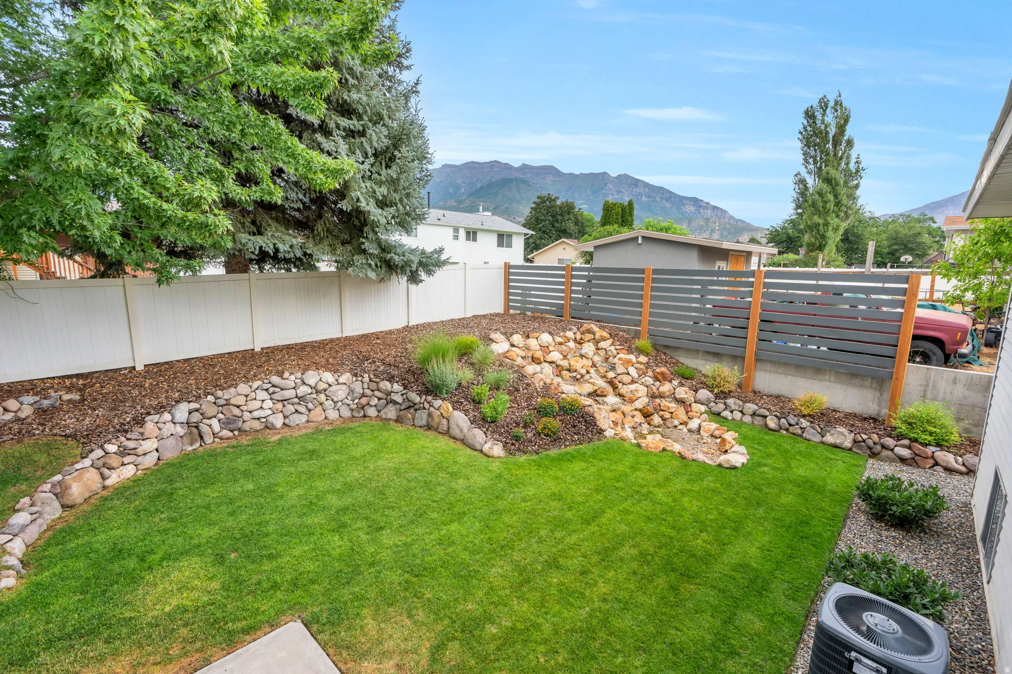 Expansive backyard featuring a lush lawn, a stone-lined planter with landscape rock and plantings, and a modern horizontal slat fence