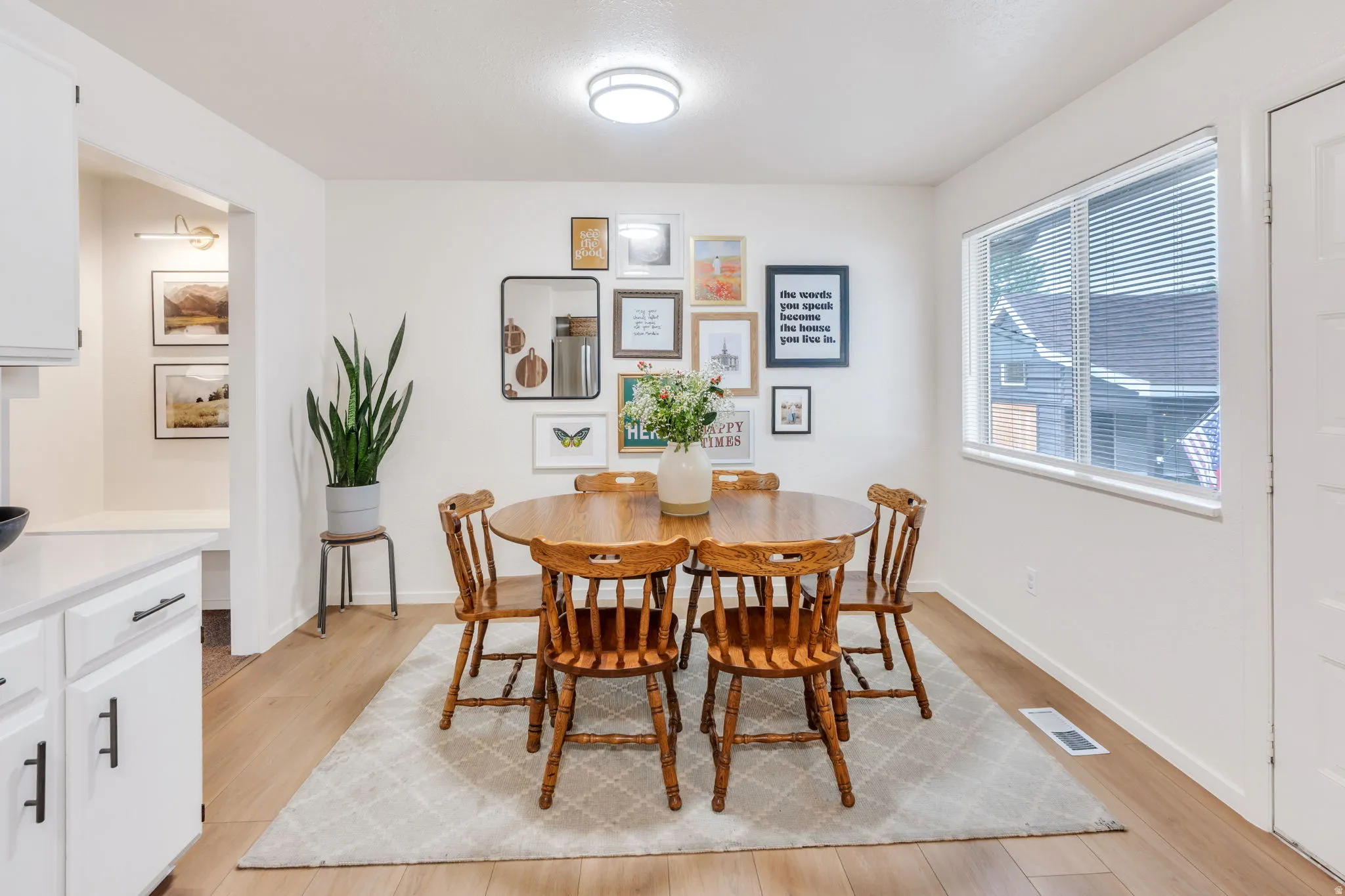 Dining area featuring wood-finish flooring, a contemporary ceiling light fixture, a window with horizontal blinds, and a built-in bench and recessed lighting visible through an archway