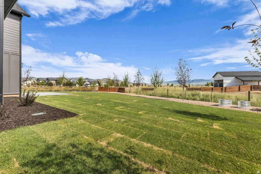 Expansive backyard featuring a manicured lawn, established landscaping beds, a gravel pathway, and a wood fence boundary