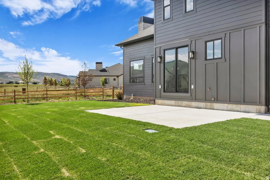 Spacious backyard featuring a concrete patio, expansive lawn, and a wood fence