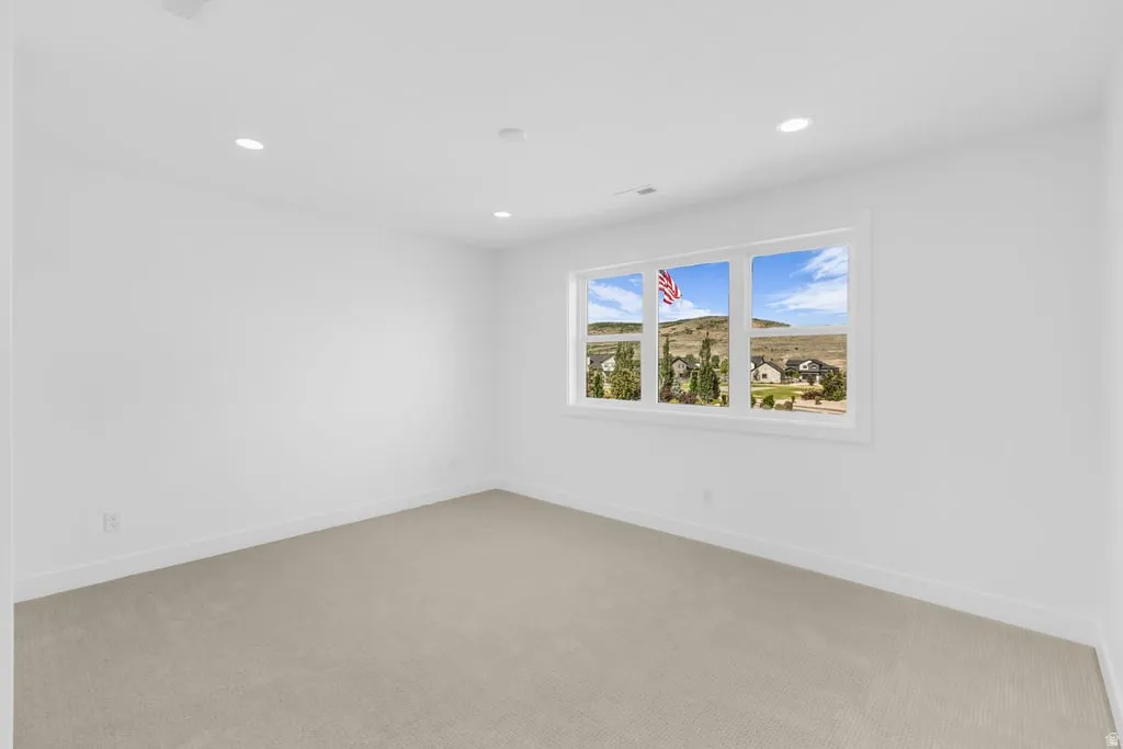 Room featuring a large multi-pane window with white trim, recessed ceiling lighting, light-toned carpet, white walls, and white baseboards